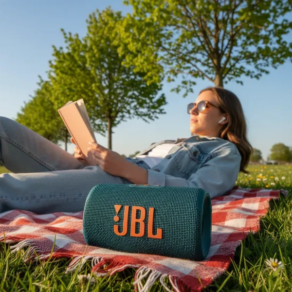 A portable Bluetooth speaker playing music outdoors, next to a person enjoying nature.